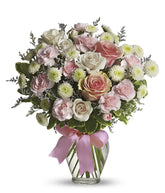 Floral arrangement featuring pink roses, white roses, mini carnations, and green poms in a clear glass vase with a bow.