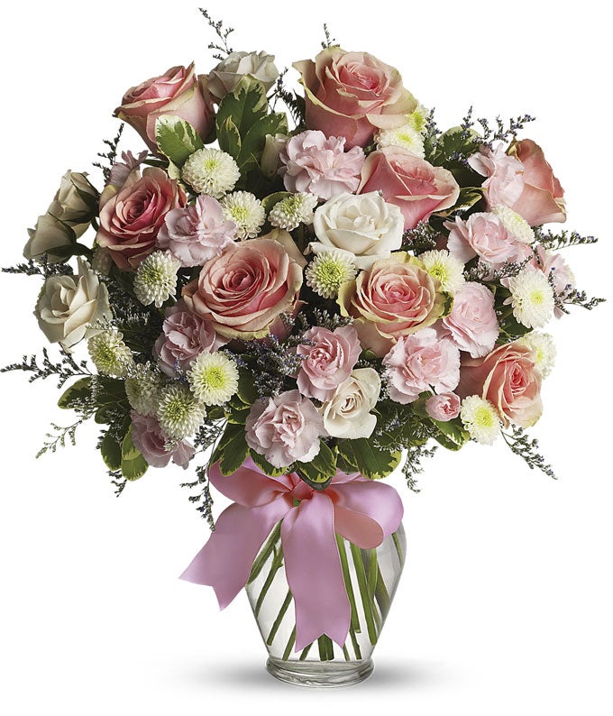 Floral arrangement featuring pink roses, white roses, mini carnations, and green poms in a clear glass vase with a bow.