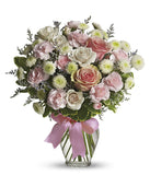 Floral arrangement featuring pink roses, white roses, mini carnations, and green poms in a clear glass vase with a bow.