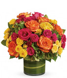 A floral arrangement featuring green hydrangea, hot pink roses, yellow roses, and bi-color roses in a clear glass vase.