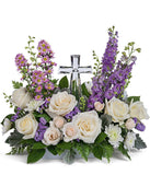 A graceful floral arrangement showcasing crème roses, lavender larkspur, lavender asters, lavender statice, white mums, and floral greens, elegantly accented with a crystal cross. This bouquet blends soft, calming colors for a serene display.