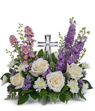 A graceful floral arrangement showcasing crème roses, lavender larkspur, lavender asters, lavender statice, white mums, and floral greens, elegantly accented with a crystal cross. This bouquet blends soft, calming colors for a serene display.