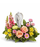 Arrangement featuring peach roses, yellow alstroemeria, yellow carnations, hot pink snapdragons, pink asters, and floral greenery with a ceramic figurine atop the arrangement 
