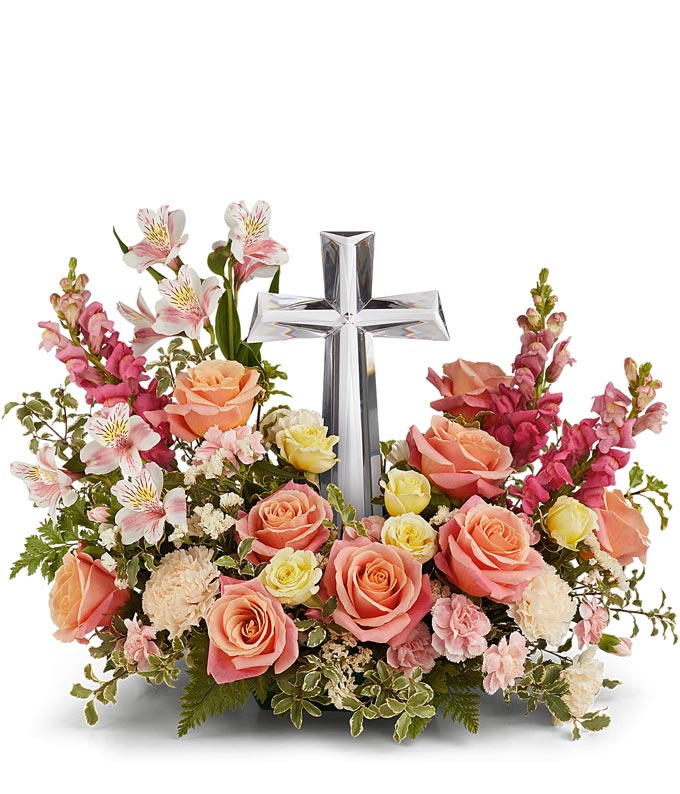 Coral roses, yellow spray roses, pink alstroemeria, creme carnations, mini pink carnations, hot pink snapdragons, and floral greenery with a large crystal cross on top of the arrangement