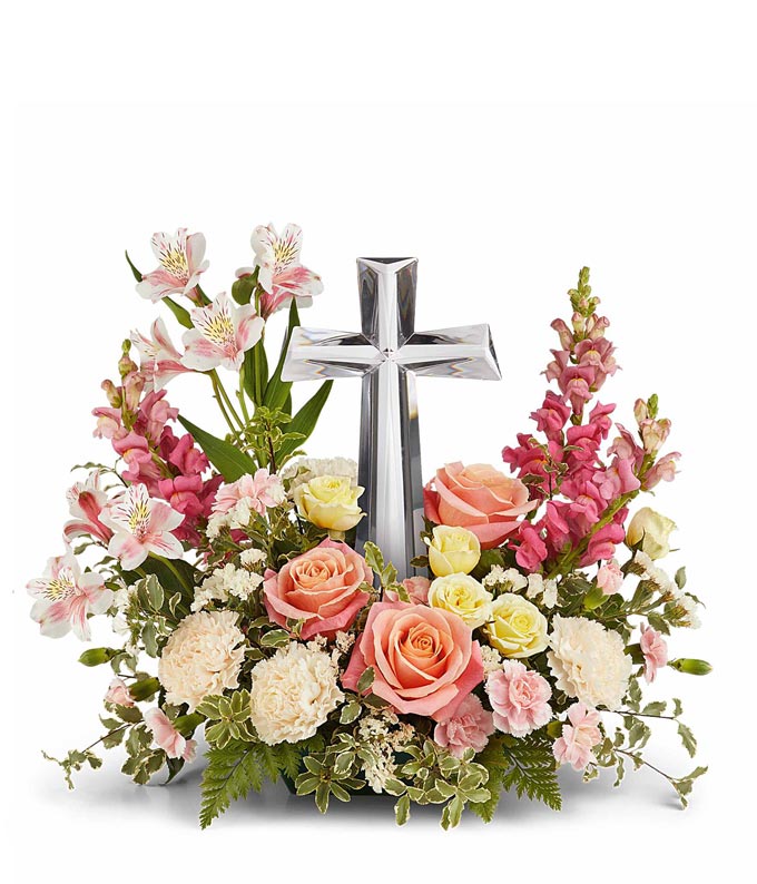 Coral roses, yellow spray roses, pink alstroemeria, creme carnations, mini pink carnations, hot pink snapdragons, and floral greenery with a large crystal cross on top of the arrangement