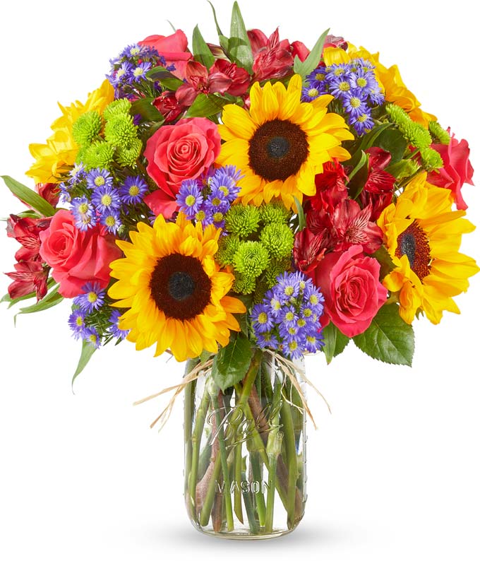 Floral arrangement featuring sunflowers, red alstroemeria, pink roses (in deluxe and premium versions), purple monte casino, and green button poms in a mason jar vase, with a personalized card message.