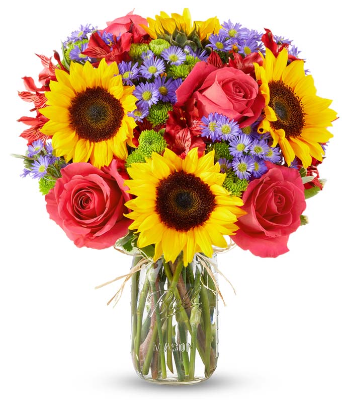 Floral arrangement featuring sunflowers, red alstroemeria, pink roses (in deluxe and premium versions), purple monte casino, and green button poms in a mason jar vase, with a personalized card message.