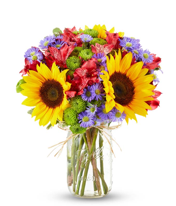 Floral arrangement featuring sunflowers, red alstroemeria, pink roses (in deluxe and premium versions), purple monte casino, and green button poms in a mason jar vase, with a personalized card message.