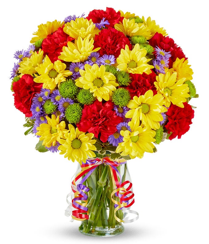 Yellow daisies, red carnations and green button poms in a glass vase