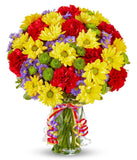 Yellow daisies, red carnations and green button poms in a glass vase