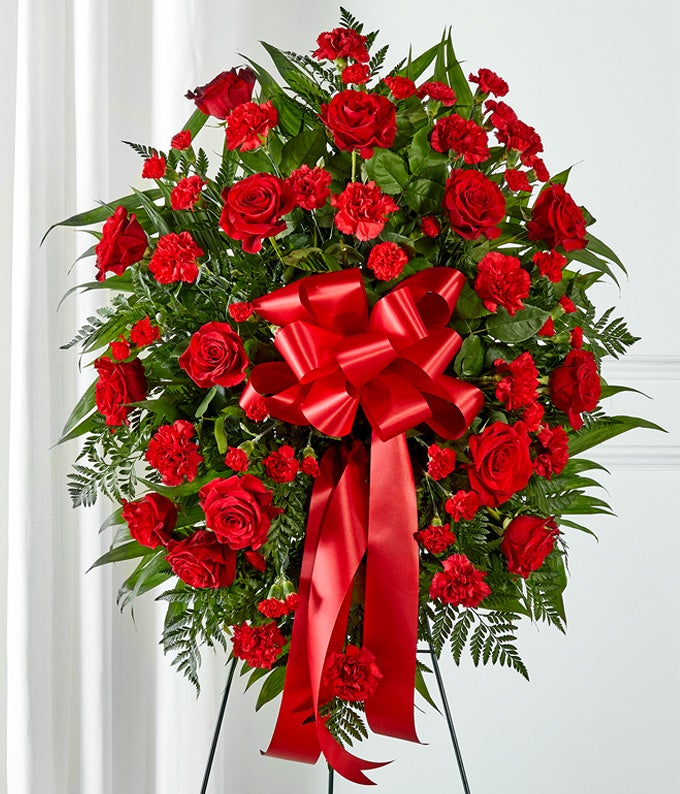 A heartfelt standing spray featuring red roses and carnations with floral greens, arranged by your local florist and hand-delivered with a decorative red bow.